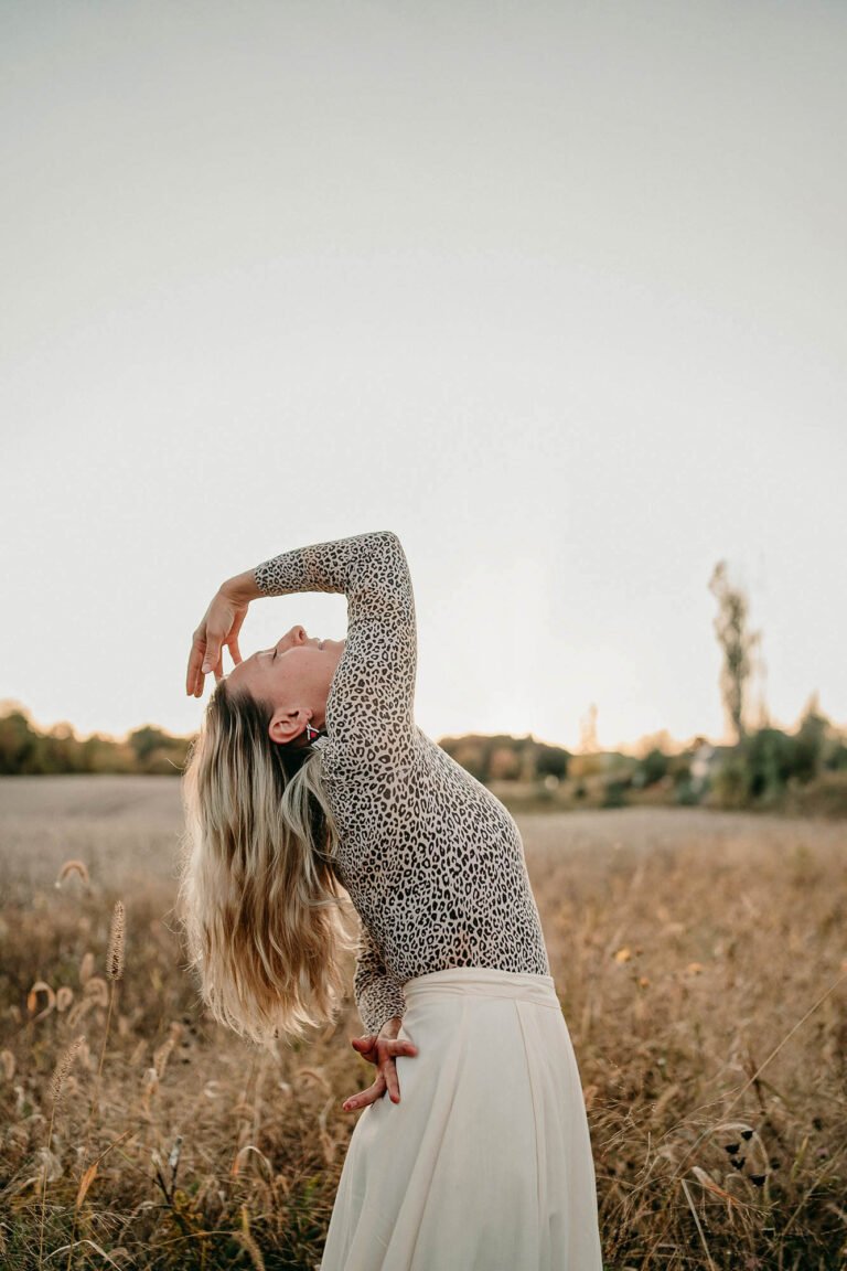 woman in sunny field dancing with hand over head